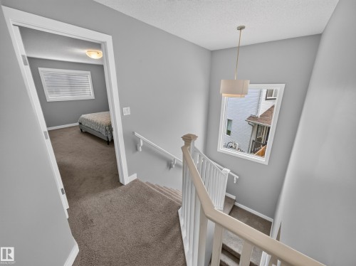 Carpeted staircase with white railings, a drum pendant light fixture, and a window with white trim - 6504 48 Avenue, Beaumont, AB - Indoor Photo Showing Other Room