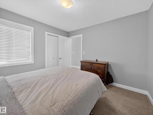 Carpeted room featuring a double-door closet, window with white blinds, and overhead flush mount lighting - 6504 48 Avenue, Beaumont, AB - Indoor Photo Showing Bedroom