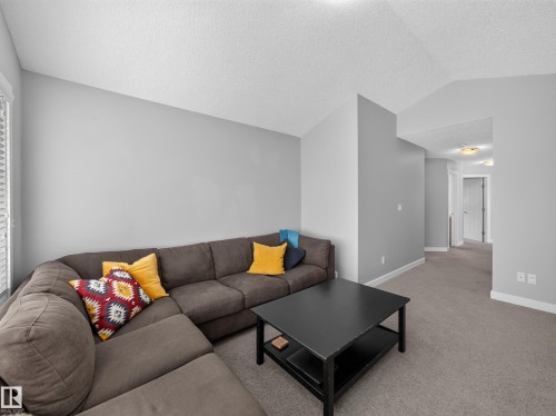 Spacious carpeted room featuring light gray walls, white baseboards, and a textured white ceiling - 6504 48 Avenue, Beaumont, AB - Indoor Photo Showing Living Room