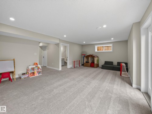 Spacious lower-level room featuring light gray carpeting, recessed ceiling lighting, a white-framed window, and a white interior door leading to an additional space - 6504 48 Avenue, Beaumont, AB - Indoor Photo Showing Basement