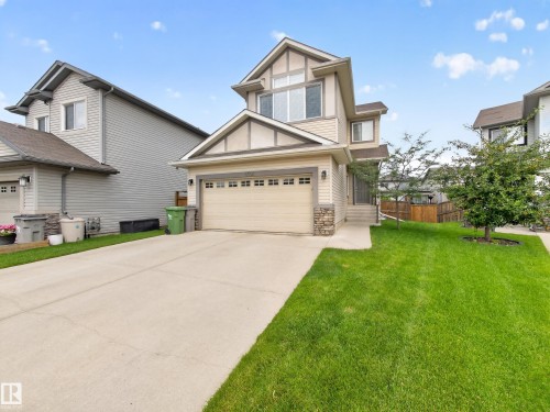 Contemporary residential exterior featuring neutral-toned siding, stone accents, a two-car garage, multiple windows, and a landscaped front yard with a concrete driveway - 6504 48 Avenue, Beaumont, AB - Outdoor