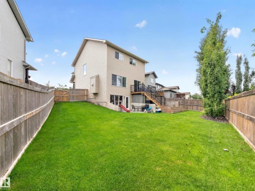 Expansive, fully fenced backyard featuring a substantial grassy lawn, a multi-level wood deck with black railings, and a concrete patio at the walk-out basement level - 6504 48 Avenue, Beaumont, AB - Outdoor With Backyard With Exterior