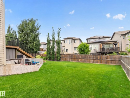 Expansive green lawn with a curved concrete patio, a multi-level wooden deck with black metal railings, a wooden privacy fence, and mature trees - 6504 48 Avenue, Beaumont, AB - Outdoor With Backyard