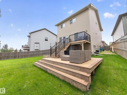 Rear exterior featuring a multi-level wood deck with black metal railings, a ground-level patio, and a spacious green lawn - 6504 48 Avenue, Beaumont, AB - Outdoor With Deck Patio Veranda With Backyard With Exterior