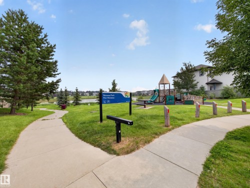 Concrete pathways winding through green lawns, bordering a park area with a playground structure - 6504 48 Avenue, Beaumont, AB - Outdoor