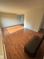 Spacious interior room featuring wood-finish flooring, light-colored walls, and a textured ceiling - 
