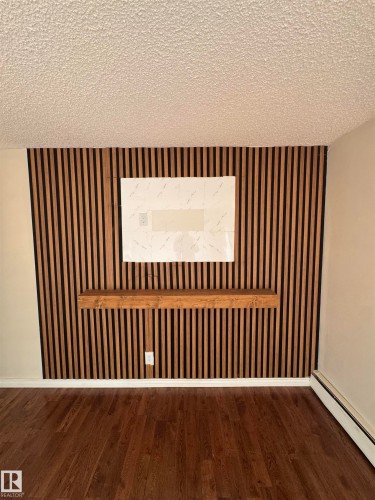 Feature wall with vertical wood slat detailing, an integrated floating wood shelf, and a ceiling-mounted baseboard heater - #205 10140 151 St Nw, Edmonton, AB - Indoor Photo Showing Other Room