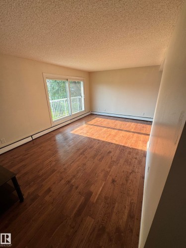 Spacious room featuring wood-finish flooring, light-toned walls, and a textured ceiling - #205 10140 151 St Nw, Edmonton, AB - Indoor Photo Showing Other Room