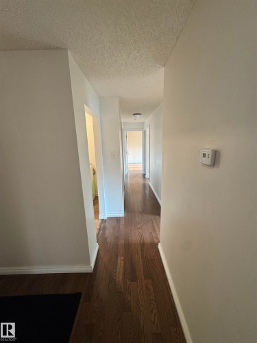 Long hallway featuring dark wood-finish flooring, white baseboards, and neutral wall paint - #205 10140 151 St Nw, Edmonton, AB - Indoor Photo Showing Other Room