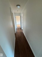 Hallway featuring dark wood-finish flooring, white walls, and a flush-mount ceiling light - 
