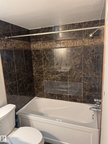 Bathtub and shower combination featuring dark marble-look wall tiles with a decorative mosaic band - #205 10140 151 St Nw, Edmonton, AB - Indoor Photo Showing Bathroom