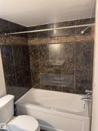 Bathtub and shower combination featuring dark marble-look wall tiles with a decorative mosaic band - 