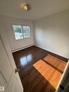 Room featuring wood-finish flooring, white painted walls, a window with exterior views, white baseboards, and a flush mount ceiling light - 