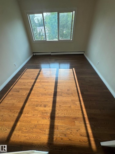 Expansive wood-finish flooring with a natural grain pattern - #205 10140 151 St Nw, Edmonton, AB - Indoor Photo Showing Other Room