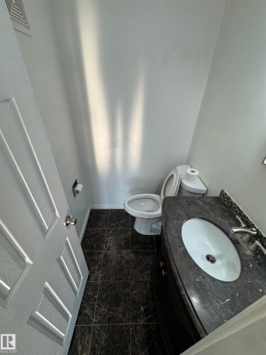 Compact bathroom featuring dark marble-look floor tiling, a vanity with a dark countertop and integrated sink, chrome faucet hardware, and a white paneled door - #205 10140 151 St Nw, Edmonton, AB - Indoor Photo Showing Bathroom