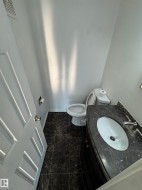 Compact bathroom featuring dark marble-look floor tiling, a vanity with a dark countertop and integrated sink, chrome faucet hardware, and a white paneled door - 