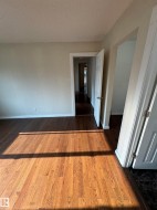 Hardwood flooring throughout featuring a light-toned wall finish, white trim, and interior doors - 
