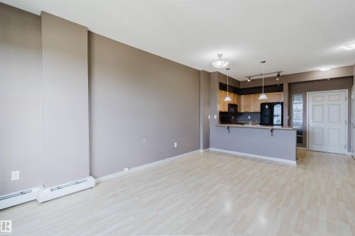 Light wood-finish flooring throughout, featuring a kitchen with wood-finish cabinetry, black appliances, and pendant lighting - #1-405 4245 139 Av Nw, Edmonton, AB 