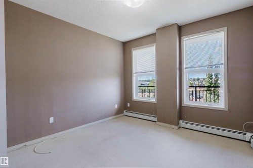 Neutral-toned walls complementing plush carpeting and two large windows fitted with blinds - #1-405 4245 139 Av Nw, Edmonton, AB 