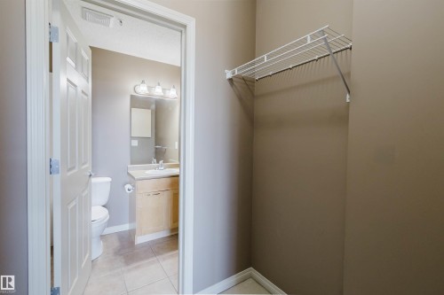 Wire shelving, light wood-finish vanity with a single sink, vanity lighting with three fixtures, and a white toilet - #1-405 4245 139 Av Nw, Edmonton, AB 