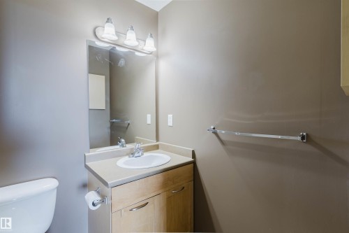 Light wood-finish vanity with an integrated sink, polished chrome faucet, and a wall-mounted mirror with overhead lighting - #1-405 4245 139 Av Nw, Edmonton, AB 