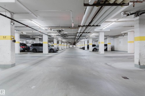 Spacious underground parking facility with concrete flooring, structural support columns, and overhead utility piping - #1-405 4245 139 Av Nw, Edmonton, AB 