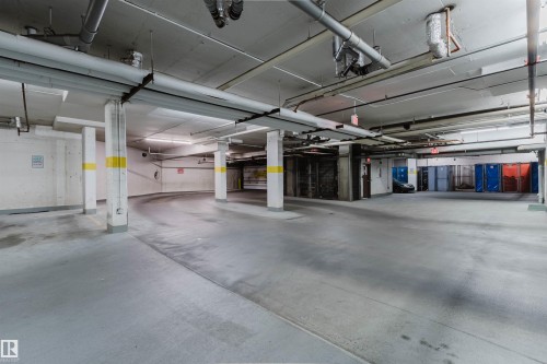 Underground parking facility with concrete flooring, support columns, overhead piping, and fluorescent lighting - #1-405 4245 139 Av Nw, Edmonton, AB 