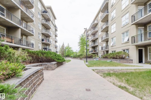 Expansive outdoor walkway featuring patterned paving stones, stone retaining walls, and mature landscaping - #1-405 4245 139 Av Nw, Edmonton, AB 