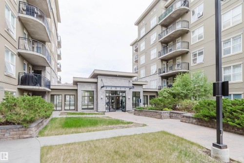 Modern building exterior featuring neutral-toned stucco, multiple balconies with black railings, and a stone-clad entrance - #1-405 4245 139 Av Nw, Edmonton, AB 