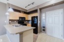 Kitchen featuring light wood cabinetry, black appliances, track lighting, and a kitchen island with integrated sink - #1-405 4245 139 Av Nw, Edmonton, AB 