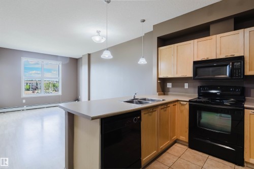 Kitchen island with a double basin stainless steel sink, black dishwasher, and pendant lighting - #1-405 4245 139 Av Nw, Edmonton, AB 