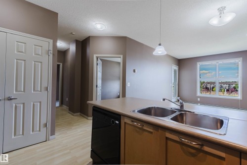 Kitchen island with double stainless steel sink, wood-finish cabinetry, and integrated dishwasher - #1-405 4245 139 Av Nw, Edmonton, AB 