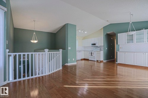 Wood-finish flooring, white kitchen cabinetry with glass panel inserts, white appliances, and a white balustrade - 15031 135 Street Nw, Edmonton, AB 