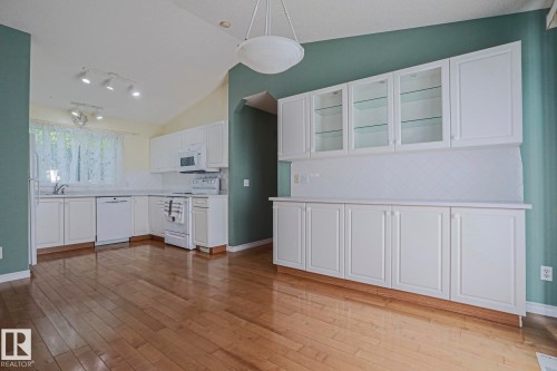 Hardwood-finish flooring, vaulted ceiling, white cabinetry with glass-front uppers, white appliances, and a tiled backsplash - 15031 135 Street Nw, Edmonton, AB 