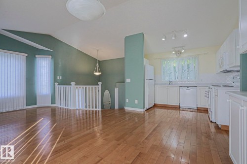 Open-concept living area with vaulted ceilings, wood-finish flooring, and a kitchen featuring white cabinetry and appliances - 15031 135 Street Nw, Edmonton, AB 