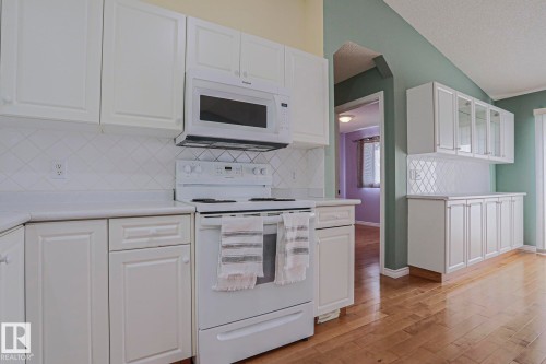 White cabinetry with brushed nickel hardware, white appliances, diagonal tile backsplash, and wood-finish flooring - 15031 135 Street Nw, Edmonton, AB 