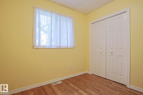 Wood-finish flooring with white trim, a window, and a built-in bifold closet - 15031 135 Street Nw, Edmonton, AB 