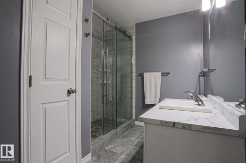 Vanity with integrated sink and chrome faucet, glass-enclosed shower with tile surround, and tile flooring - 15031 135 Street Nw, Edmonton, AB 