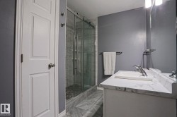 Vanity with integrated sink and chrome faucet, glass-enclosed shower with tile surround, and tile flooring - 
