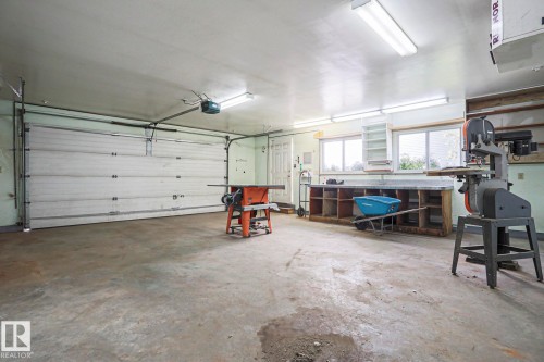 Attached garage featuring a white sectional door, concrete flooring, overhead fluorescent lighting, built-in shelving, and dual windows - 15031 135 Street Nw, Edmonton, AB 