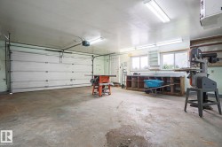 Attached garage featuring a white sectional door, concrete flooring, overhead fluorescent lighting, built-in shelving, and dual windows - 
