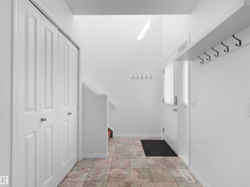 Tiled flooring, white bi-fold closet doors, integrated coat hooks, staircase with white railing, and a front entry door with privacy glass - 2410 32B Street Nw, Edmonton, AB 