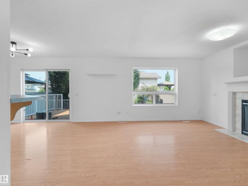 Wood-finish flooring, sliding glass door to exterior deck, and a built-in fireplace with a stone surround and mantel - 2410 32B Street Nw, Edmonton, AB 