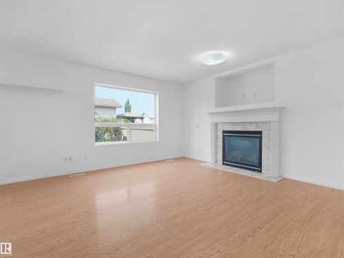 Expansive living area featuring light wood-finish flooring, a contemporary fireplace with a tiled surround, a decorative mantel, and an integrated display niche - 2410 32B Street Nw, Edmonton, AB 