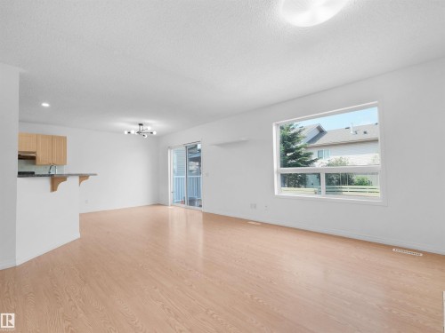Open concept living area with wood-finish flooring, ample natural light from large windows, and a sliding glass door - 2410 32B Street Nw, Edmonton, AB 