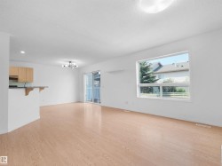 Open concept living area with wood-finish flooring, ample natural light from large windows, and a sliding glass door - 