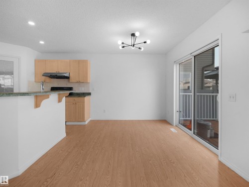Light wood-finish flooring, recessed ceiling lighting, kitchen with wood cabinetry, green countertop, and a sliding glass door - 2410 32B Street Nw, Edmonton, AB 