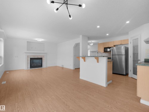Open-concept living area featuring wood-finish flooring, a contemporary chandelier, and a fireplace with a stone surround - 2410 32B Street Nw, Edmonton, AB 