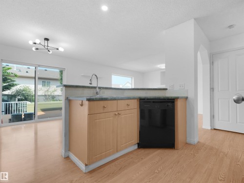 Kitchen island with a built-in sink and dishwasher, wood-finish flooring, sliding glass doors, contemporary lighting fixture, and white walls - 2410 32B Street Nw, Edmonton, AB 