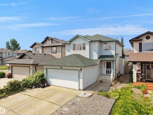 Two-story exterior with light-colored siding, contrasting dark green shingles, a single-car garage, and a concrete driveway - 2410 32B Street Nw, Edmonton, AB 